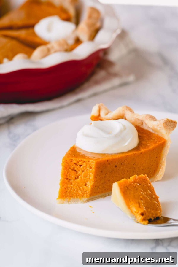 Velvet Pumpkin Dream Pie 5 A delectable slice of pumpkin pie adorned with a generous dollop of homemade whipped cream, with a small bite taken out.
