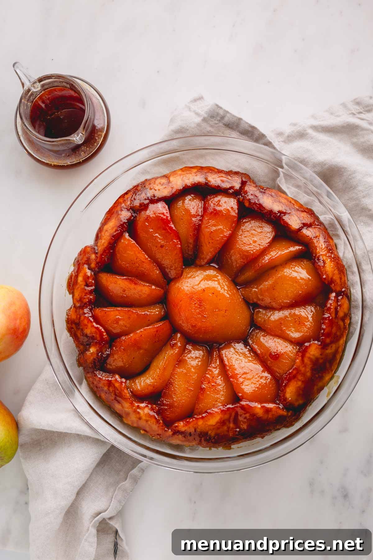 Overhead shot of a full pear tarte tatin in a glass baking dish, showcasing its golden crust and caramelized pears.