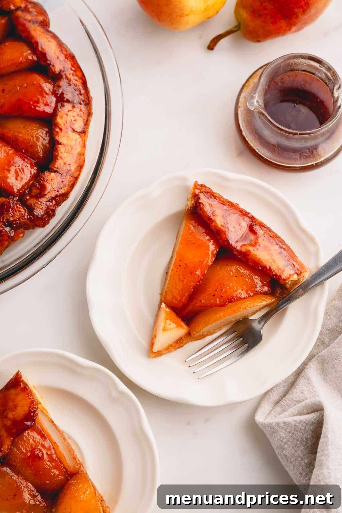 A close-up of a slice of pear tarte tatin on a plate with a fork, emphasizing its textures and inviting appearance.