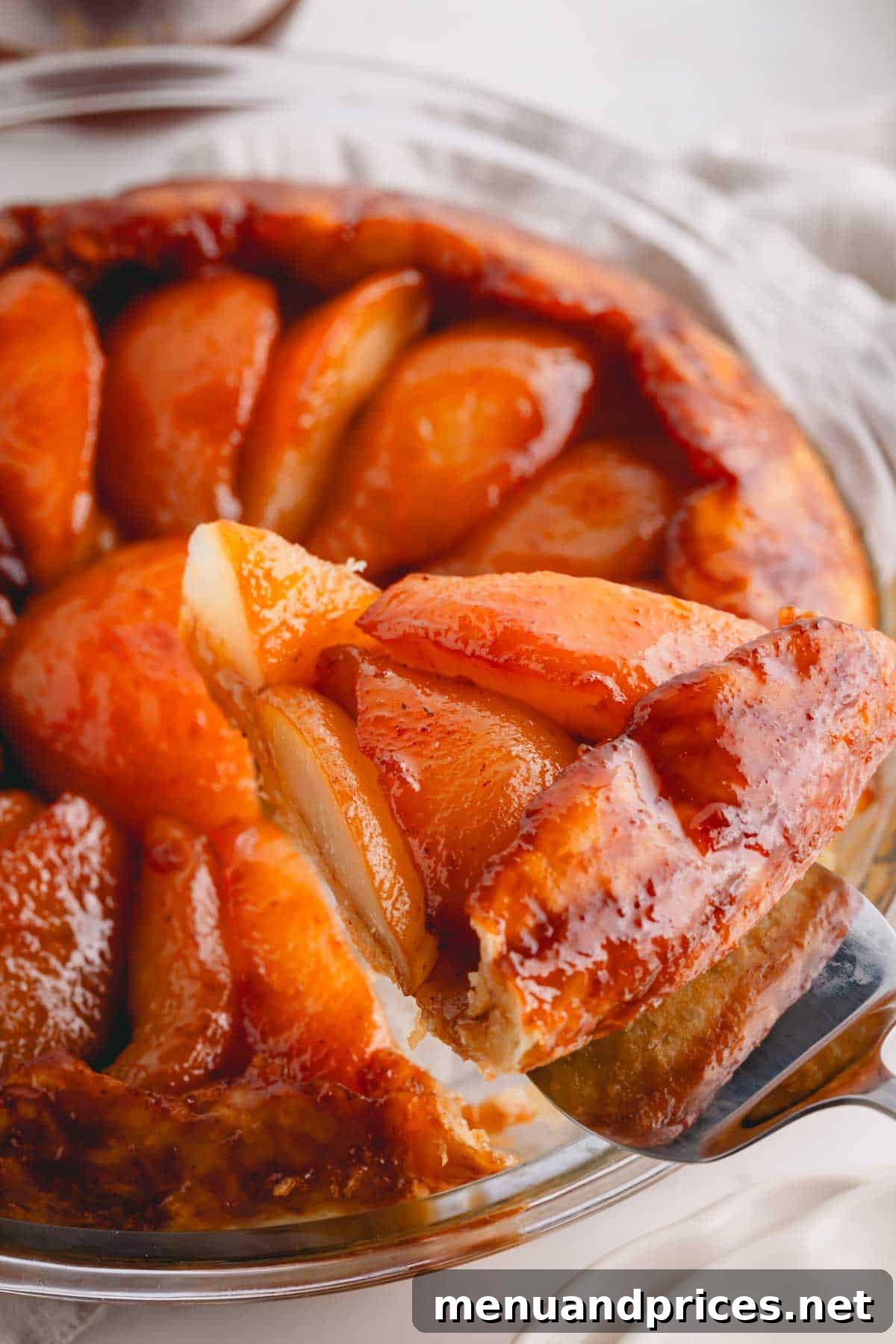 A slice of pear tarte tatin being lifted from a glass pie dish, revealing the caramelized pear layer.
