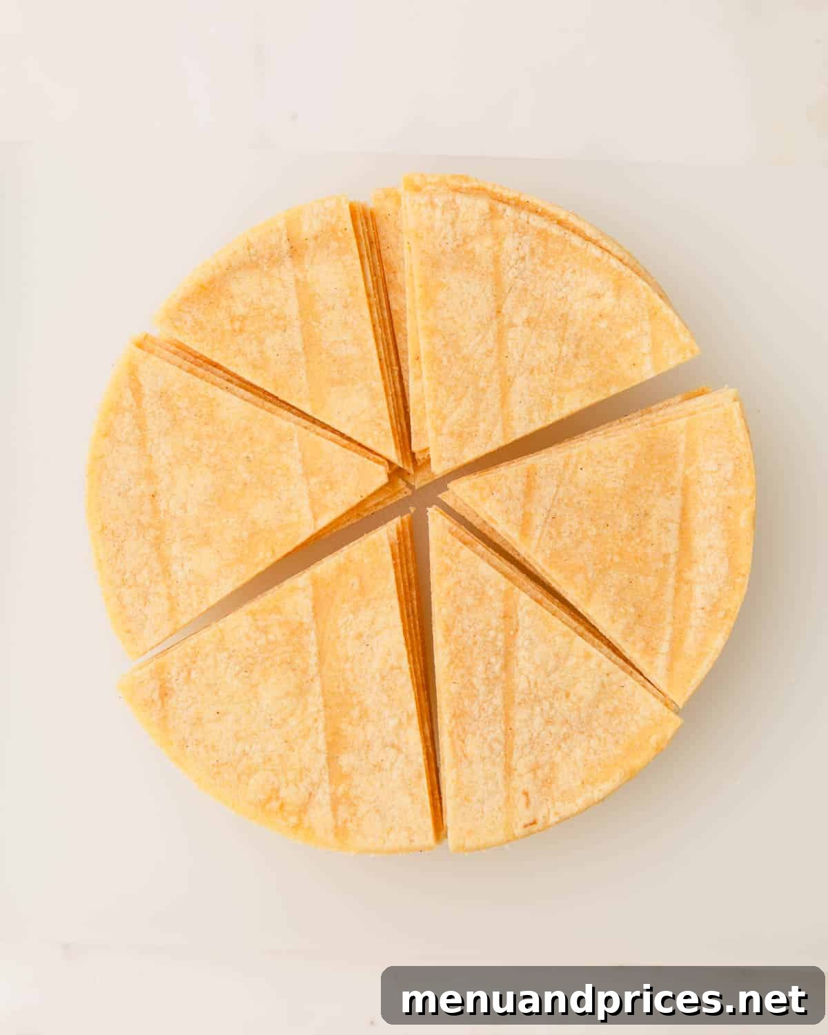 Zesty Handcrafted Tortilla Chips 5 A stack of corn tortillas precisely cut into six triangular pieces, ready for frying.