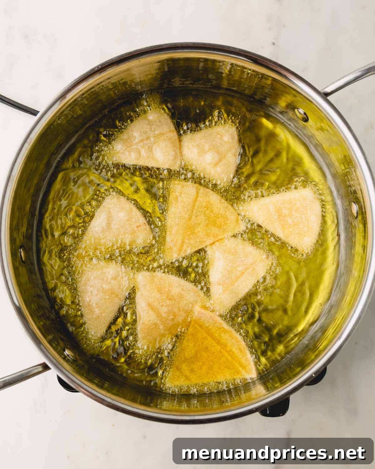 Zesty Handcrafted Tortilla Chips 6 Tortilla chip triangles frying in a heavy-bottomed pan with hot oil, bubbling around them.
