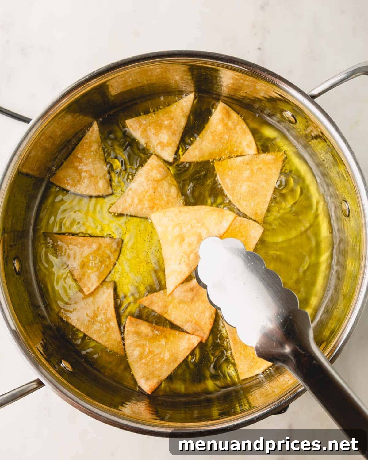 Zesty Handcrafted Tortilla Chips 7 Tongs carefully removing golden-brown tortilla chips from hot oil, demonstrating the draining process.