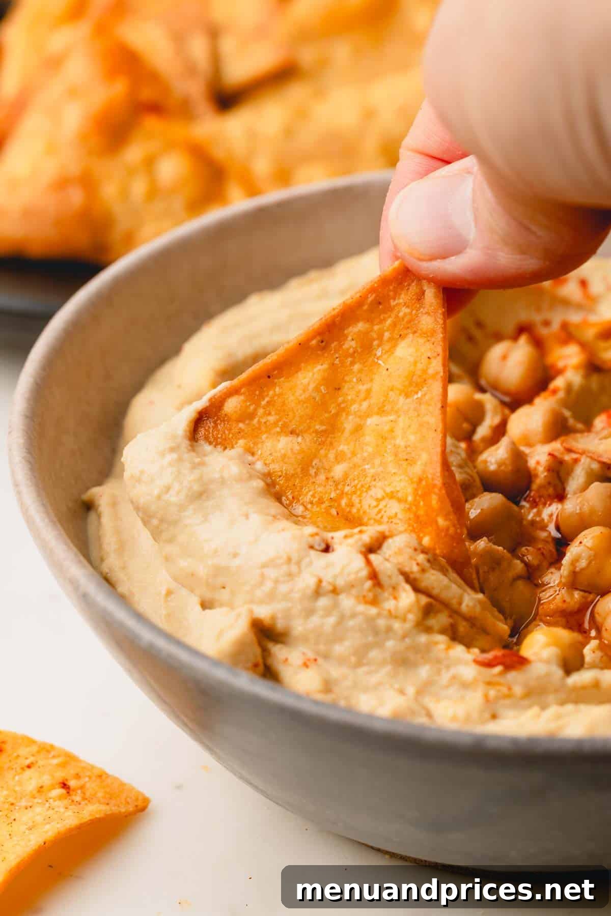 Zesty Handcrafted Tortilla Chips 9 A perfectly golden, spicy tortilla chip being dipped into a creamy bowl of hummus, showcasing its crisp texture.