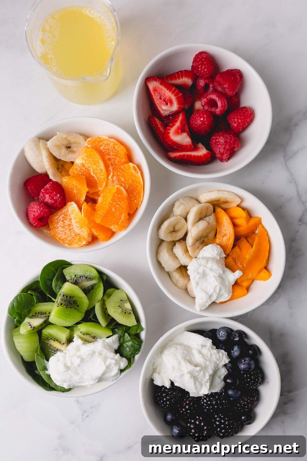 Kaleidoscope Quencher 3 Five separate bowls, each containing the prepped ingredients for one layer of the rainbow smoothie: blueberries and blackberries for purple, kiwi and spinach for green, mango for yellow, orange for orange, and raspberries and strawberries for red.