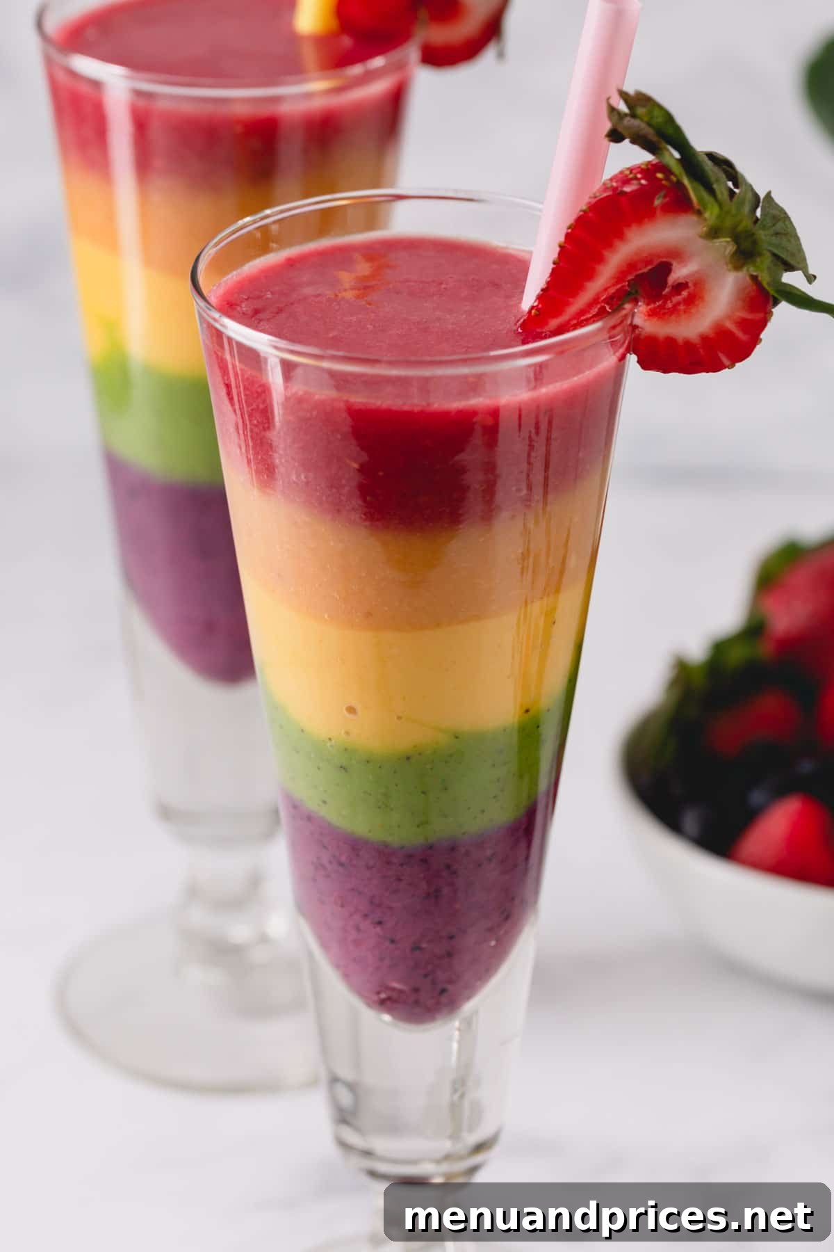 Kaleidoscope Quencher 5 Two tall glasses of perfectly layered rainbow smoothies, showcasing each vibrant color, ready to be enjoyed.