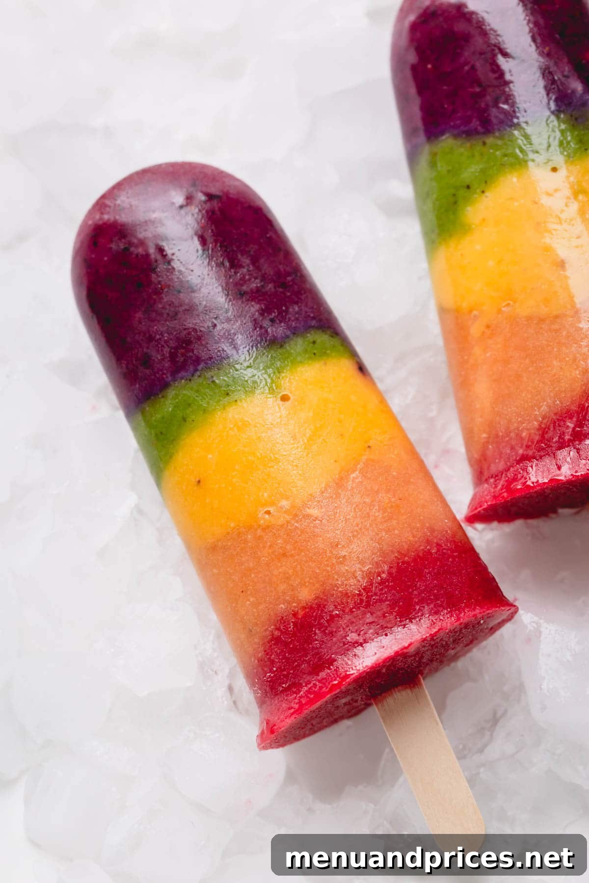 Kaleidoscope Quencher 6 Colorful rainbow popsicles arranged artfully over crushed ice, showcasing the distinct fruit layers.