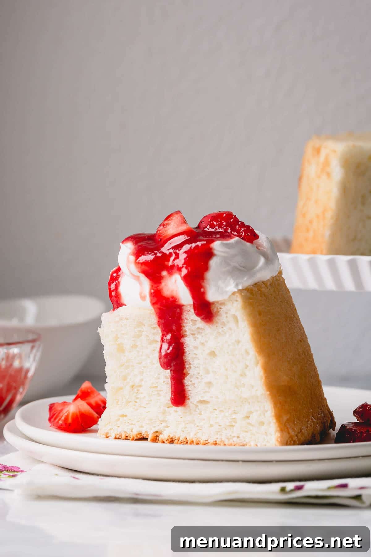 Light & Airy Angel Food Delight 2 A beautiful slice of Angel Food Cake generously topped with freshly whipped cream and a luscious strawberry sauce, presented on a pristine white plate.