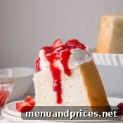 A slice of angel food cake topped with whipped cream and strawberry sauce.