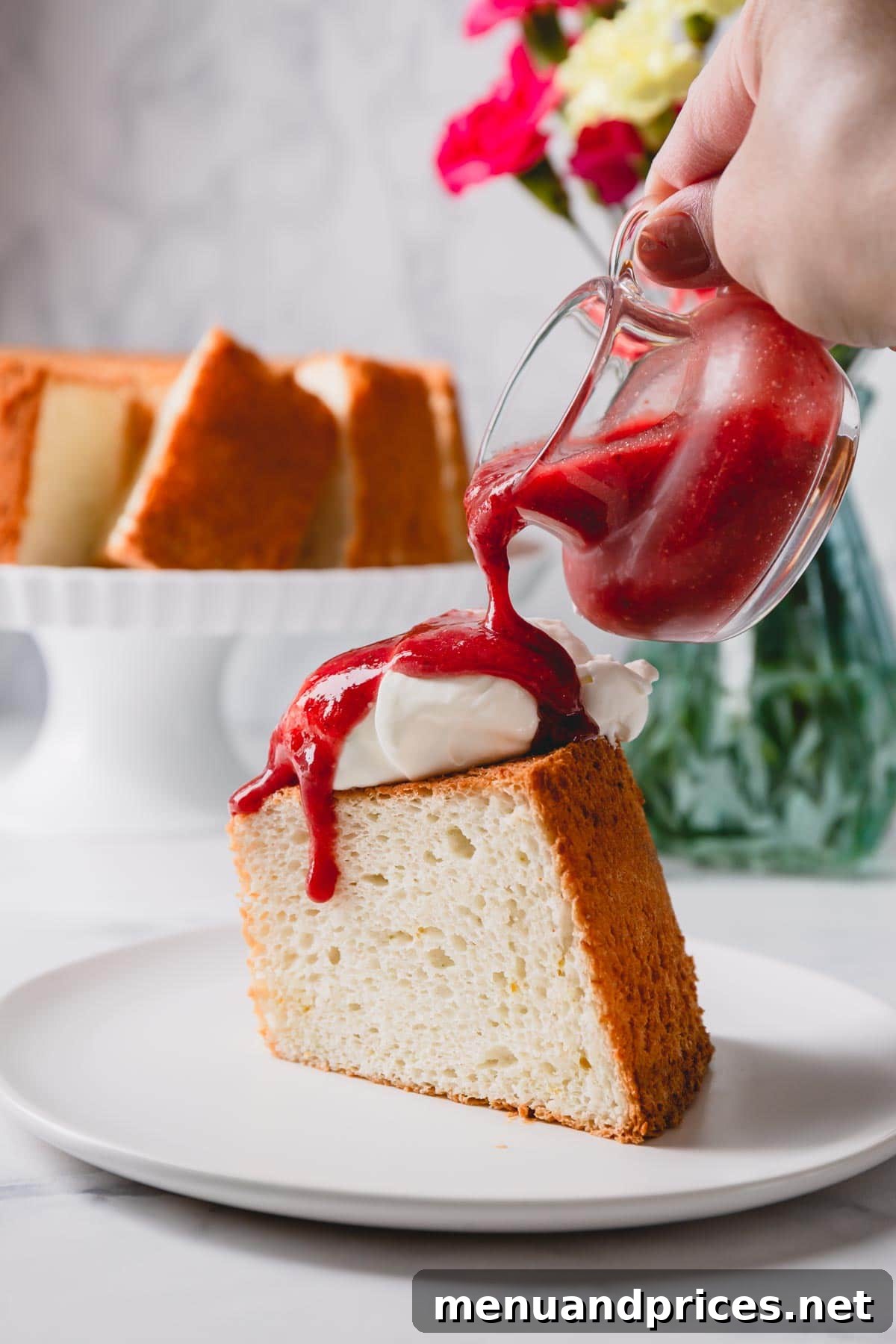Light & Airy Angel Food Delight 10 A delectable slice of Angel Food Cake, elegantly topped with fluffy whipped cream and a homemade strawberry sauce, showcasing its pristine white interior.