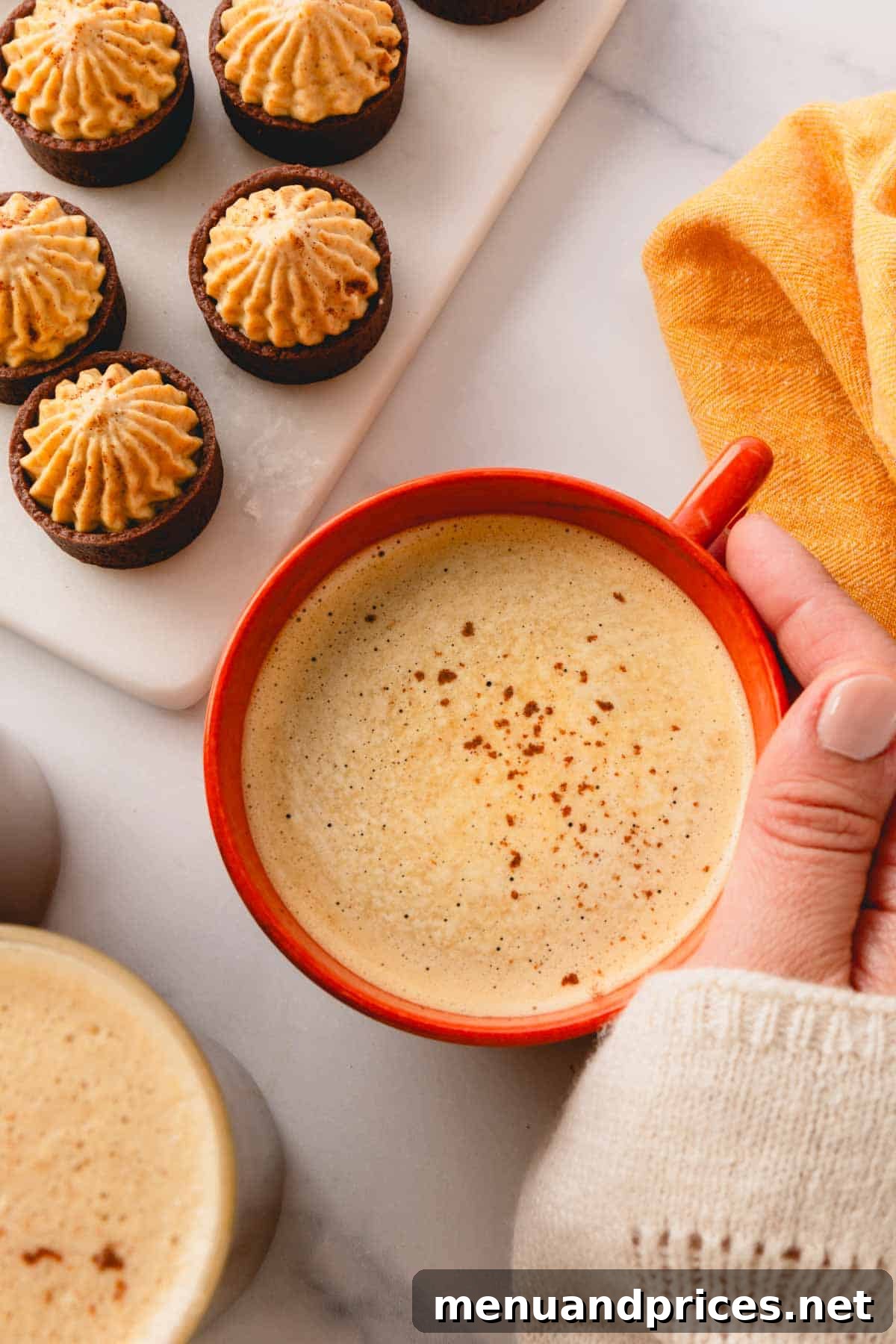 A hand holding a mug of pumpkin coffee next to chocolate cups filled with pumpkin mousse.