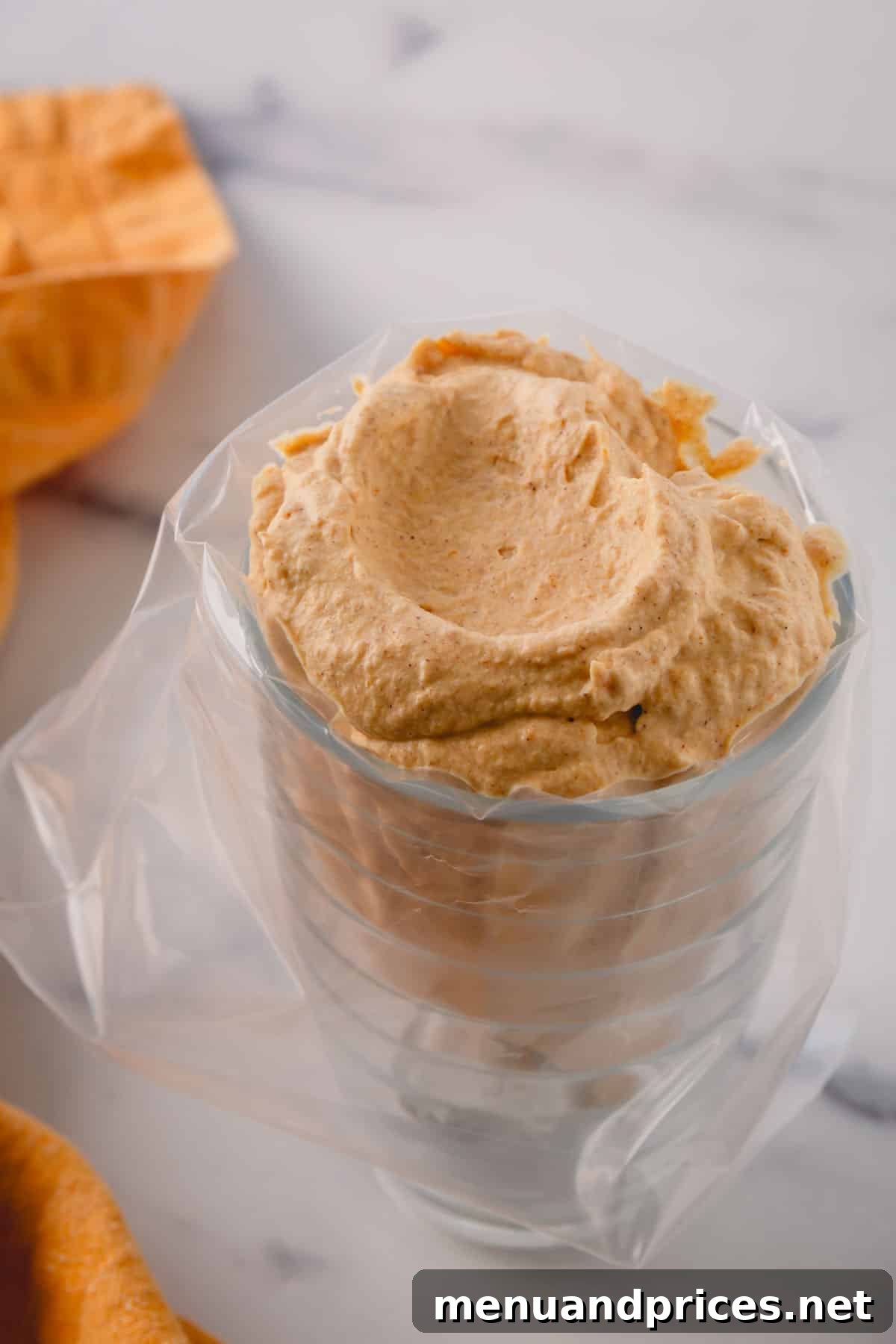 A cup covered with a bag full of pumpkin mousse.