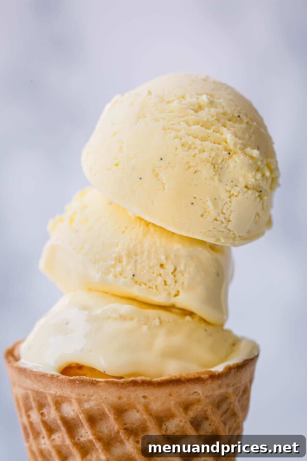 Dreamy Homemade Vanilla Ice Cream 10 Three generous scoops of homemade vanilla ice cream elegantly stacked on a crispy wafer cone, ready to be enjoyed.