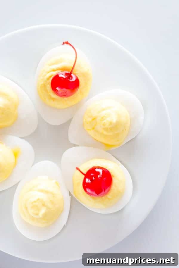 Tropical Pina Colada Deviled Eggs 4 A selection of sweet deviled eggs arranged beautifully on a white serving platter, some topped with a maraschino cherry.