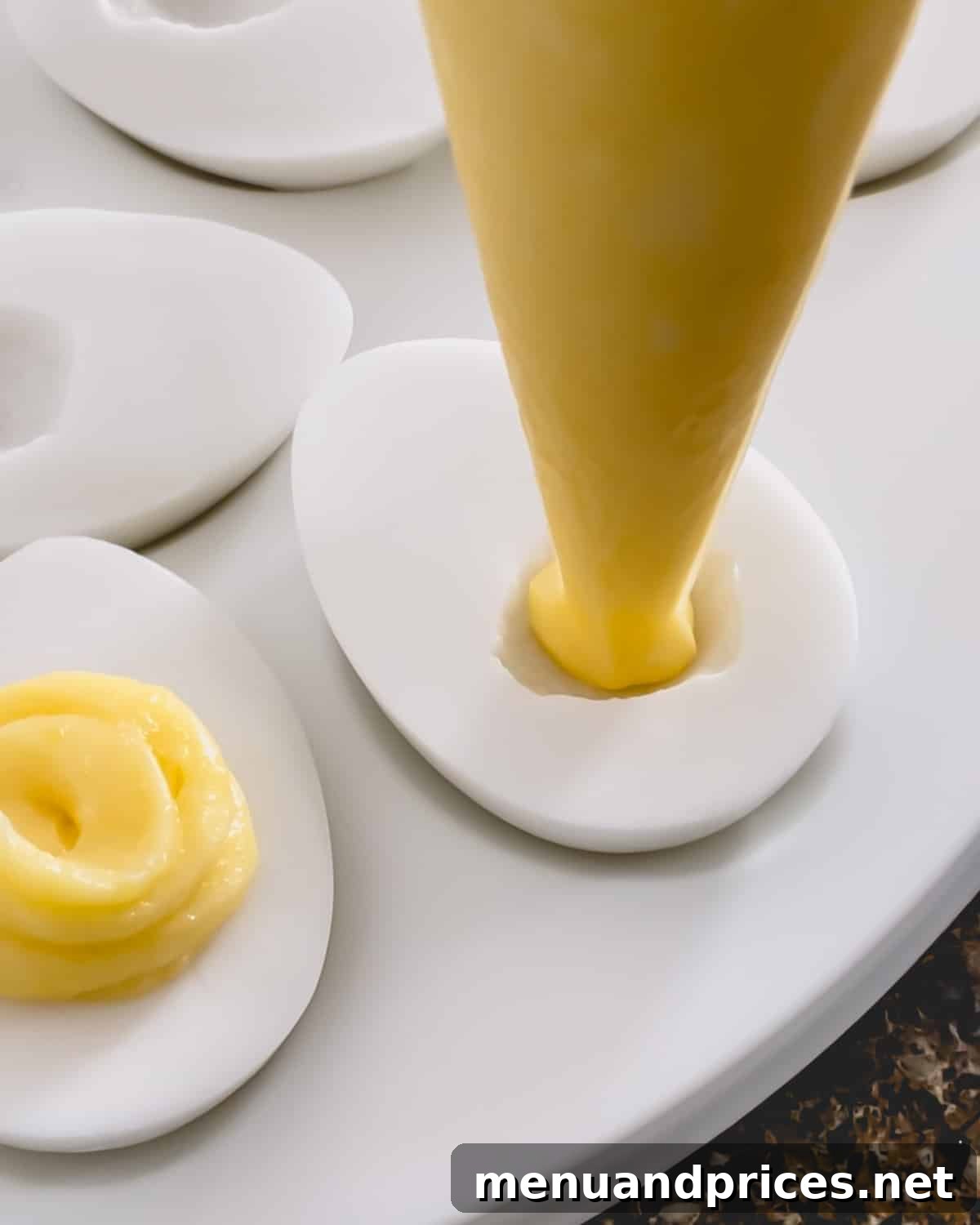 Tropical Pina Colada Deviled Eggs 10 Bright yellow pineapple filling being piped into the well of an egg-shaped coconut pudding.