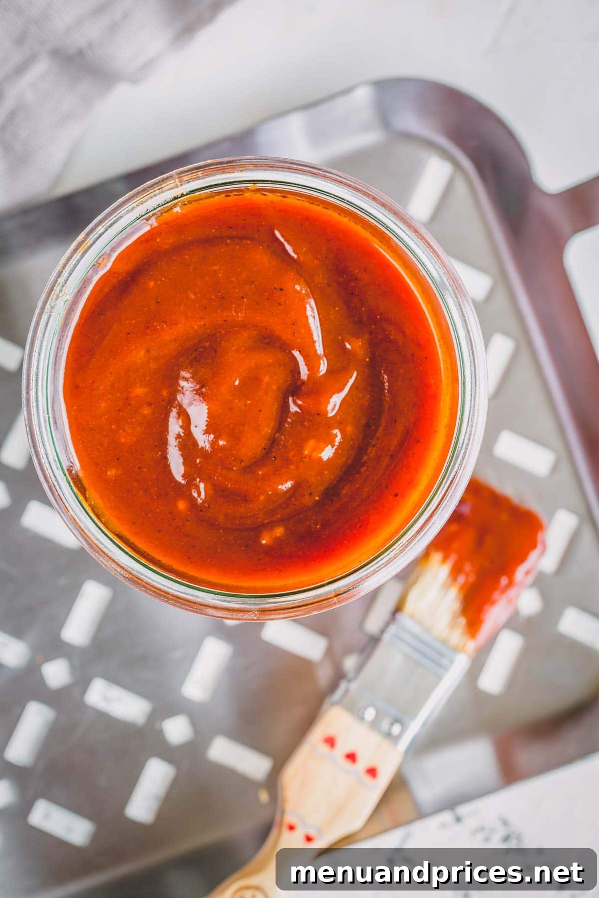 Crafting Your Perfect Homemade BBQ Sauce 4 A jar of homemade BBQ sauce sitting on a grill tray with a basting brush on the side, ready for action.
