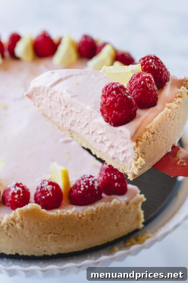 Zesty Berry No-Bake Cheesecake Bliss 3 A perfectly sliced piece of lemon raspberry no-bake cheesecake, revealing its creamy texture and crumbly crust, with a small portion already removed from the whole cake.