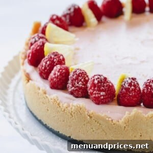 a whole lemon raspberry cheesecake topped with fresh raspberries on a white serving platter.