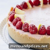 a whole lemon raspberry cheesecake topped with fresh raspberries on a white serving platter.