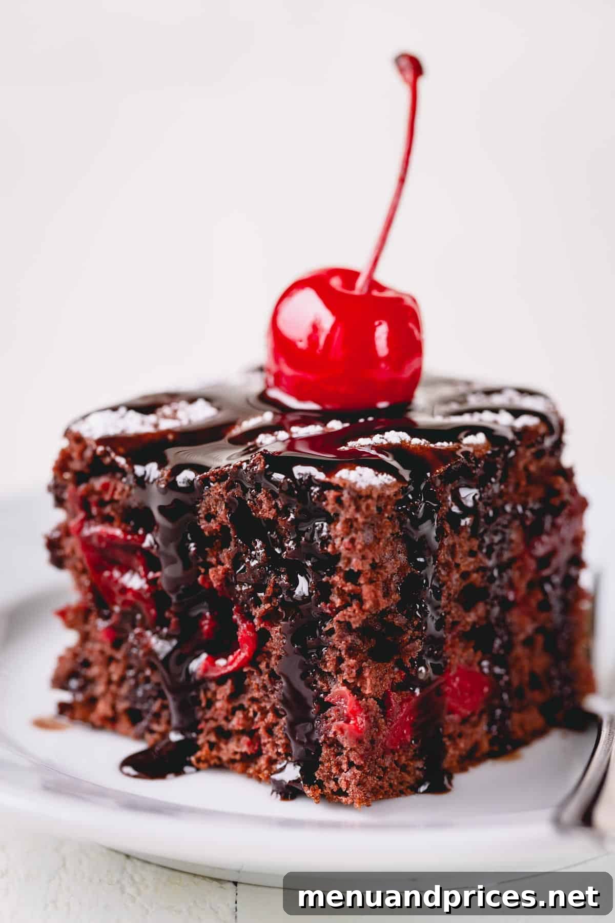 Effortless Chocolate Cherry Bliss 2 A delectable slice of chocolate cherry cake, elegantly topped with rich chocolate fudge and a vibrant maraschino cherry.