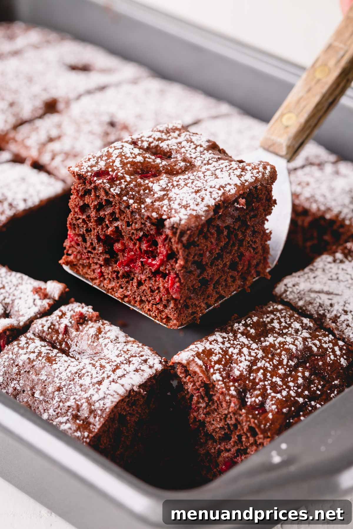 Effortless Chocolate Cherry Bliss 5 A freshly baked chocolate cherry cake resting in a baking pan, with one generous slice gracefully lifted out, revealing its moist interior and cherry pieces.