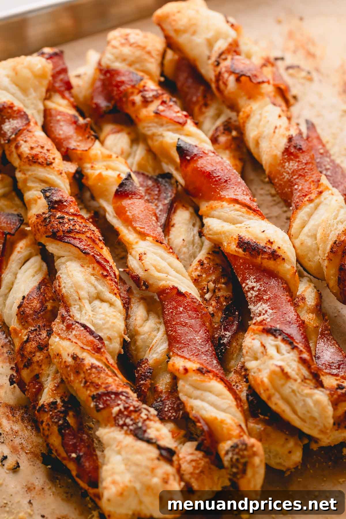 Golden Savory Spirals 3 Savory puff pastry twists with prosciutto and jam on a parchment paper lined baking sheet.
