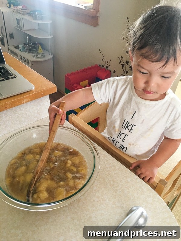 Culinary Chaos with a Curious Kid 2 Toddler boy Grant happily helping his mom make banana bread, stirring ingredients in a mixing bowl with a spoon, kitchen counter