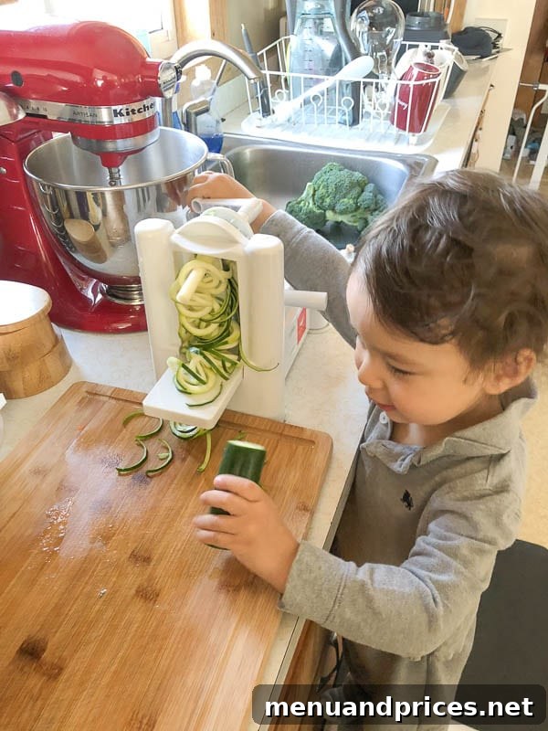 Culinary Chaos with a Curious Kid 13 Toddler boy Grant intently helping with a spiralizer to prepare zucchini and other vibrant vegetables in the kitchen, showing his handy skills