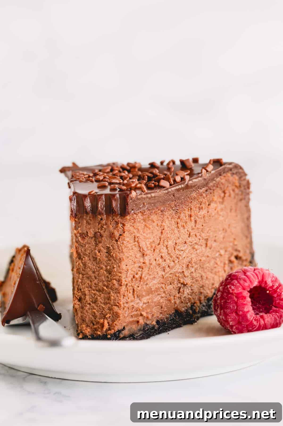 Velvet Chocolate Heaven Cheesecake 12 A perfectly cut slice of supreme chocolate cheesecake with a thick ganache topping on a white plate.