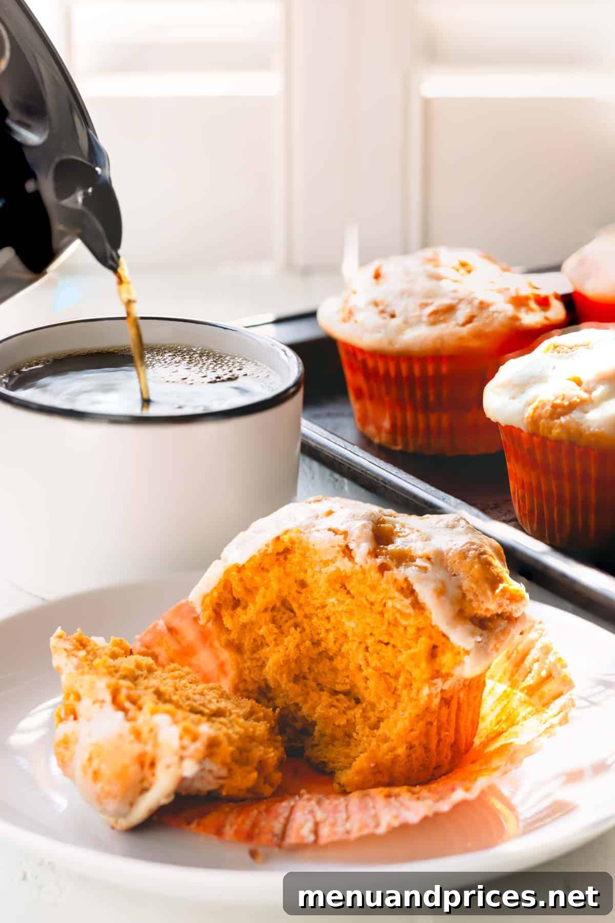 Cheesecake Swirl Pumpkin Muffins 3 A pumpkin muffin torn in half on a white plate, revealing its moist crumb and cream cheese swirl, with a mug of coffee in the background.