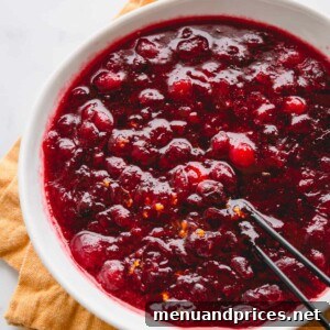 Homemade orange cranberry sauce in a white bowl, garnished with fresh cranberries and orange slices.