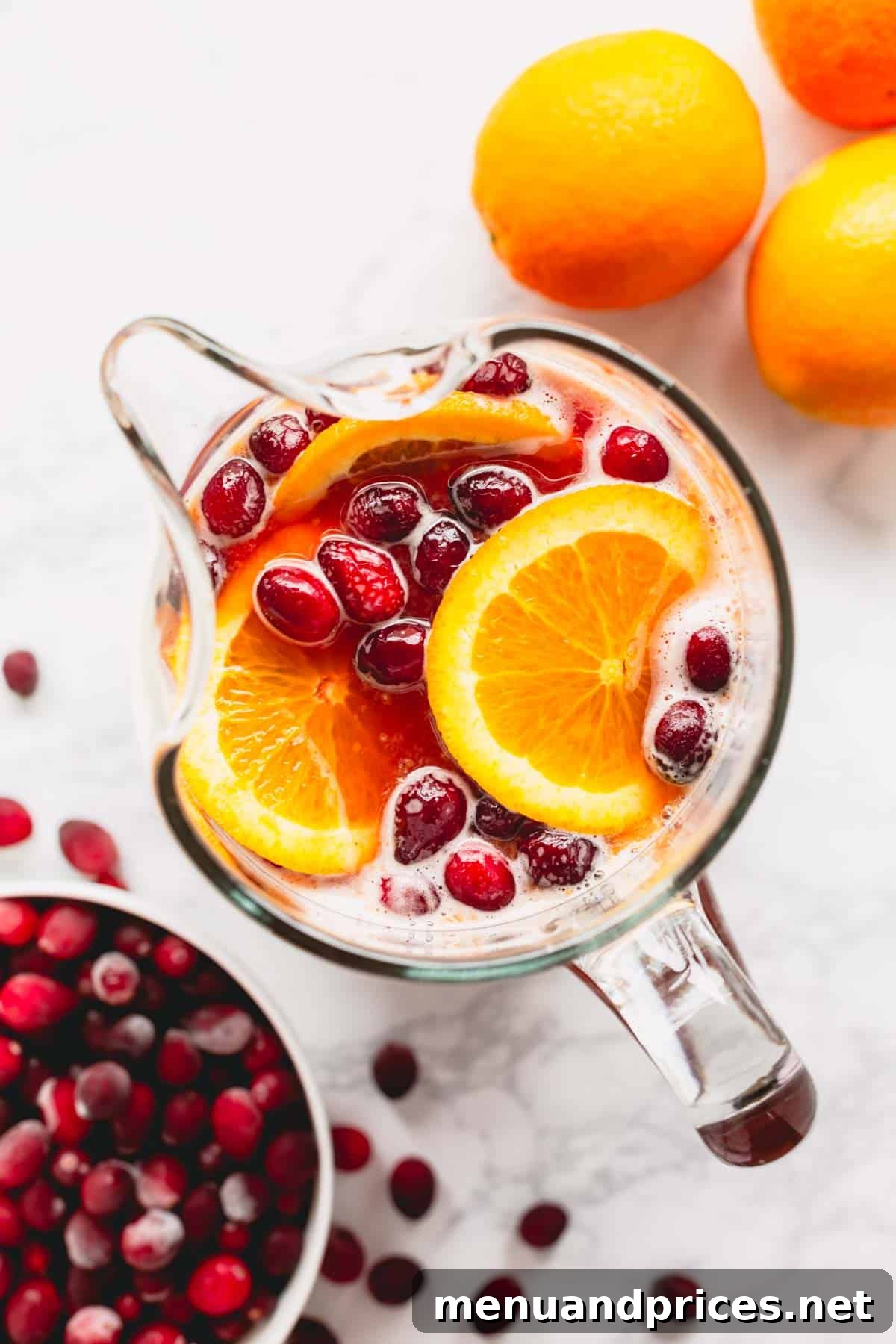 Overhead image of a pitcher of orange cranberry spritzer with pomegranates and orange slices, ready to be served.