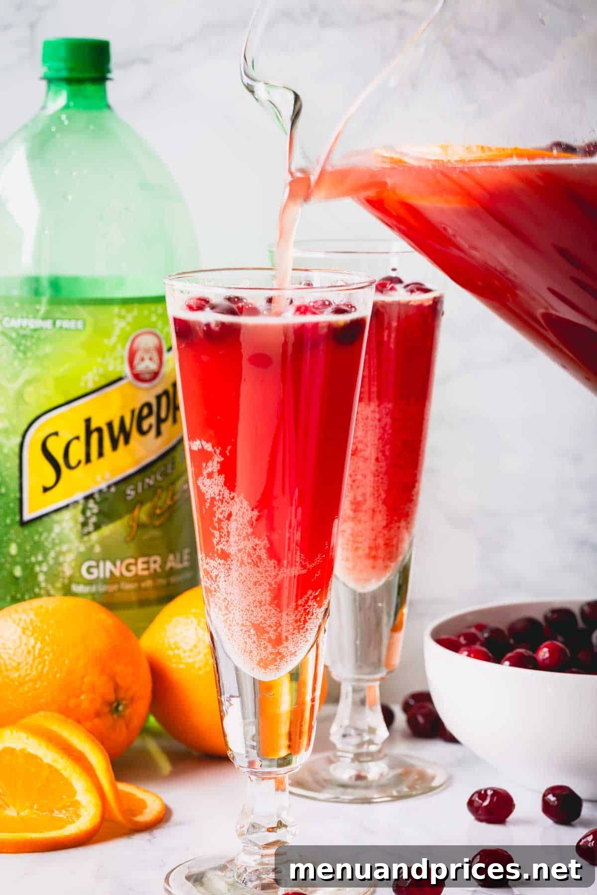 Orange cranberry spritzer being poured into two elegant glasses, showcasing its vibrant color.