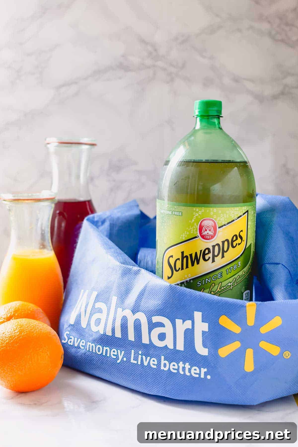 Schweppes ginger ale, two fresh oranges, a bottle of orange juice, and a bottle of pomegranate juice, with a Walmart shopping bag in the background, illustrating the key ingredients for the spritzer.