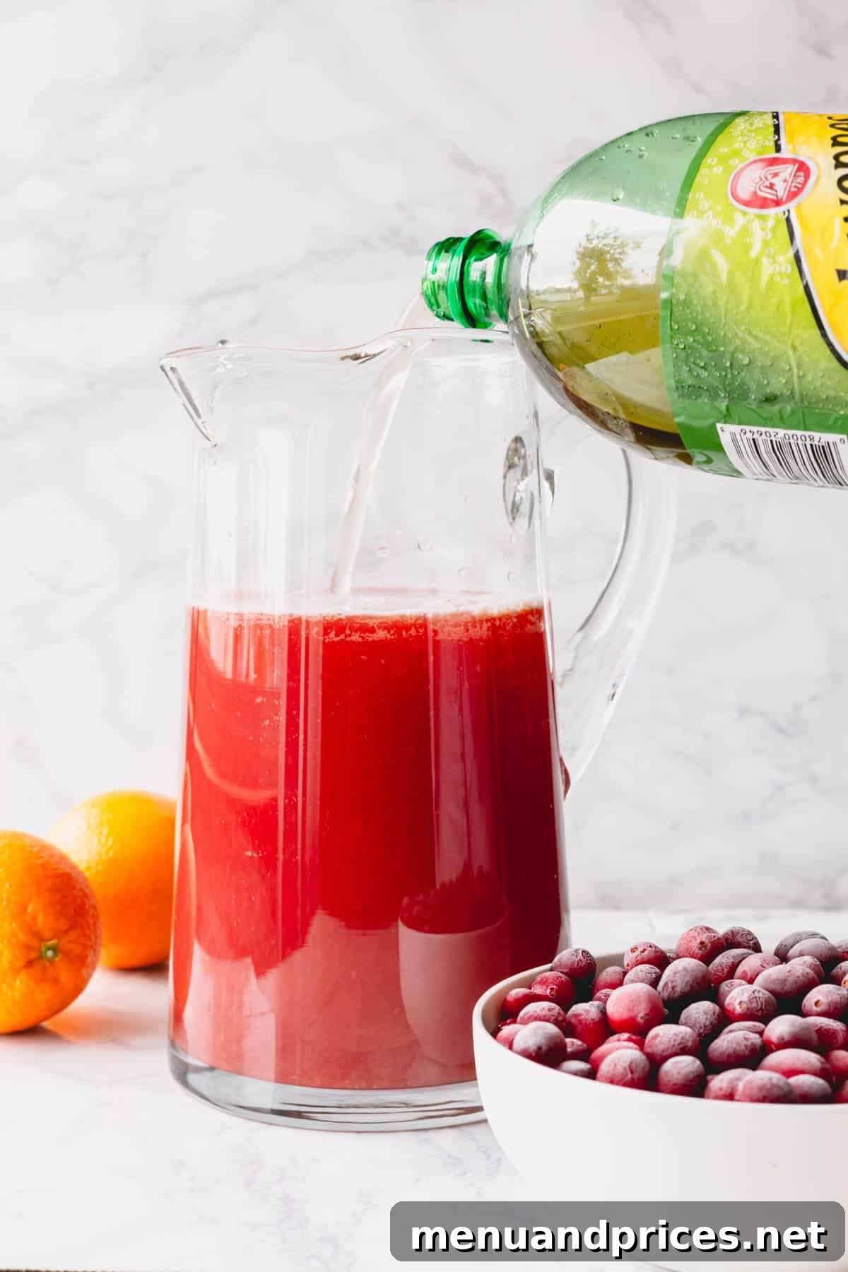 Ginger ale being poured into a pitcher of orange juice and cranberry juice, highlighting the addition of the bubbly component.
