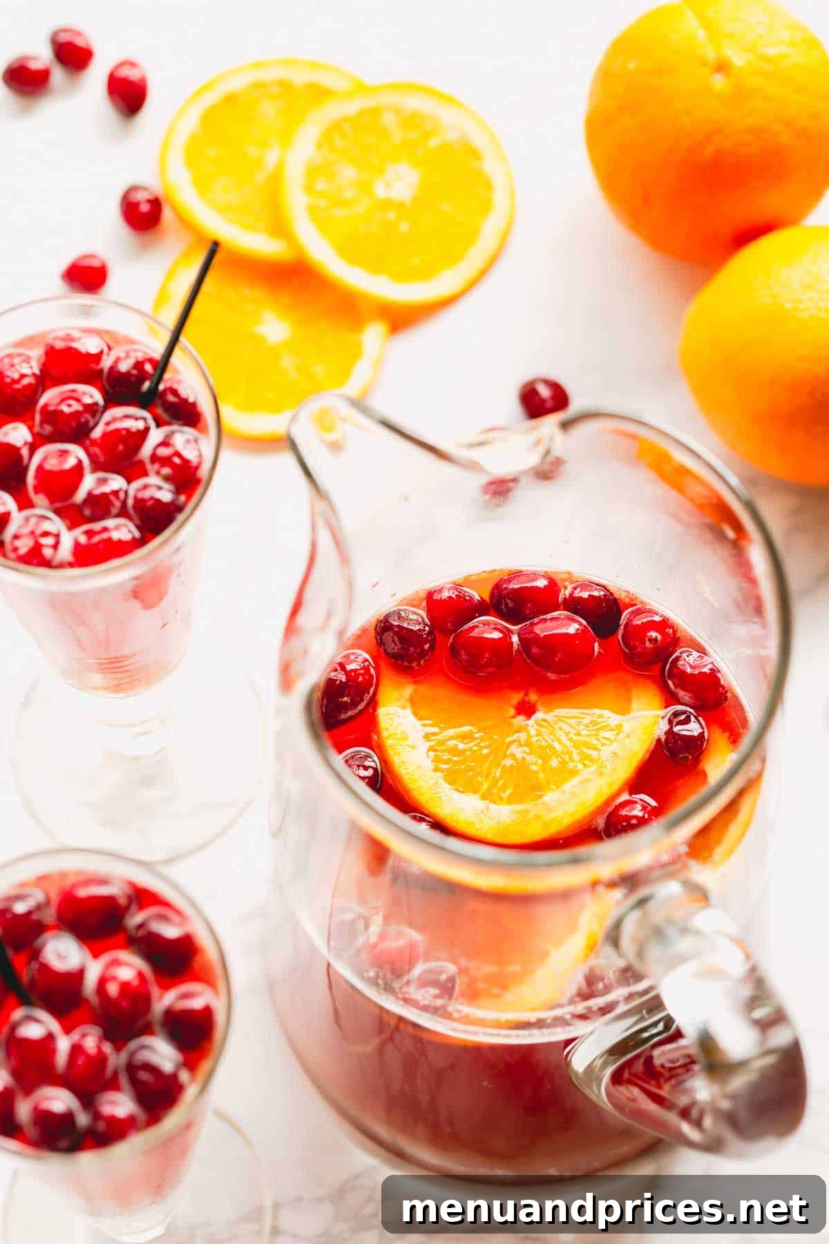 Overhead image of two glasses of orange cranberry spritzer and a pitcher of the spritzer mix, indicating a completed and ready-to-serve beverage.