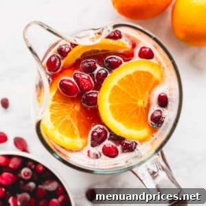 Overhead image of a pitcher of orange cranberry spritzer with pomegranates and orange slices.
