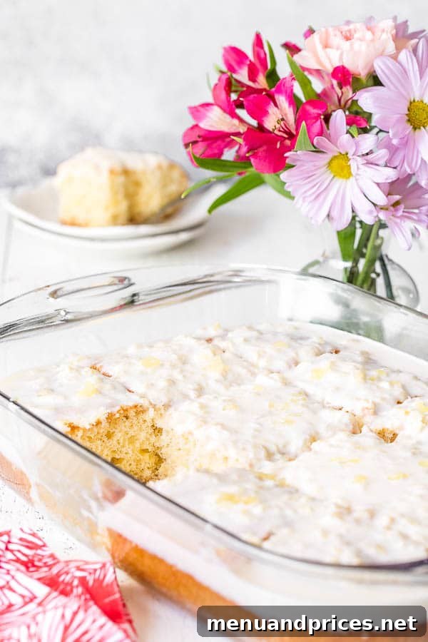 A baking dish full of frosted pineapple cake with a square piece missing.