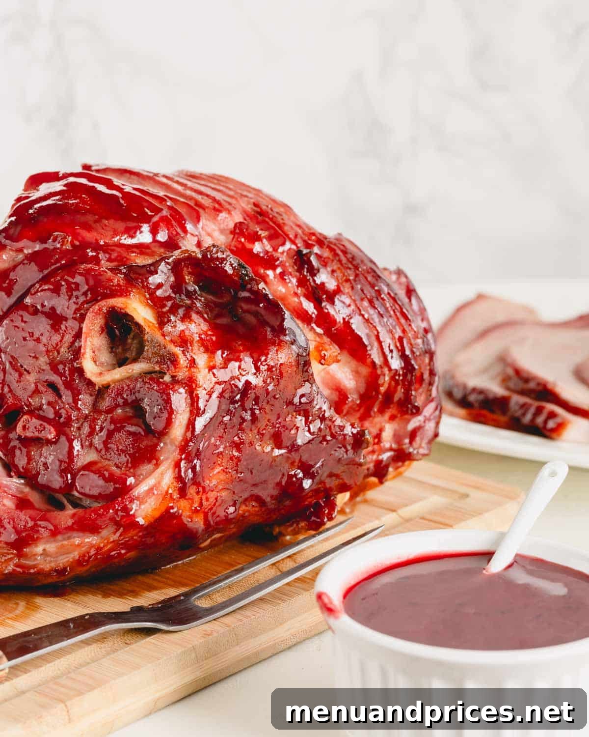 A cooked spiral ham on a cutting board next to a bowl of the 2-ingredient spiral ham glaze, inviting to be served.