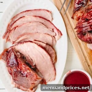 Overhead image of glazed spiral ham on a wooden cutting board and a serving platter with a bowl of glaze.