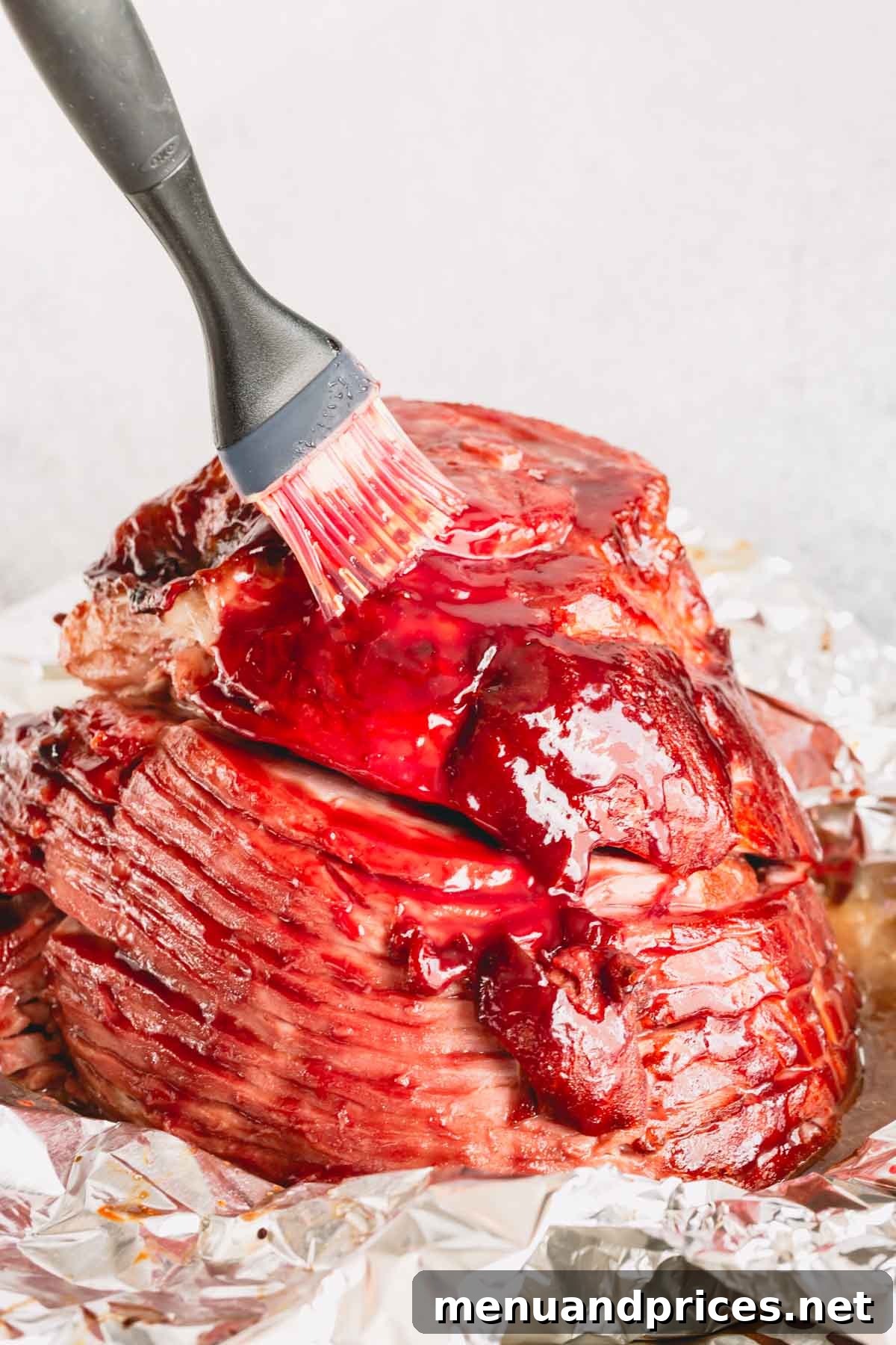A spiral ham being brushed with raspberry mustard glaze, highlighting its glossy finish just before serving.
