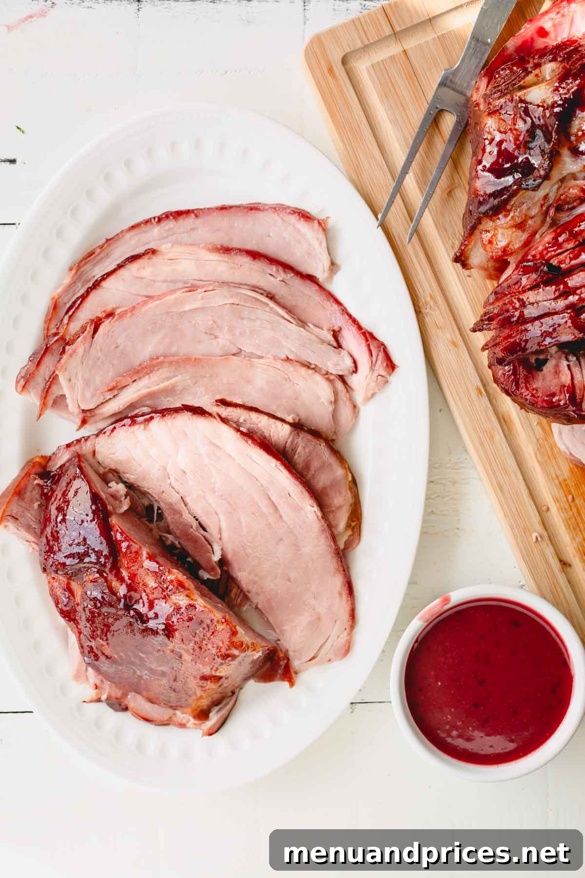 Overhead image of glazed spiral ham on a wooden cutting board and a serving platter with a bowl of glaze, showcasing its festive appeal.