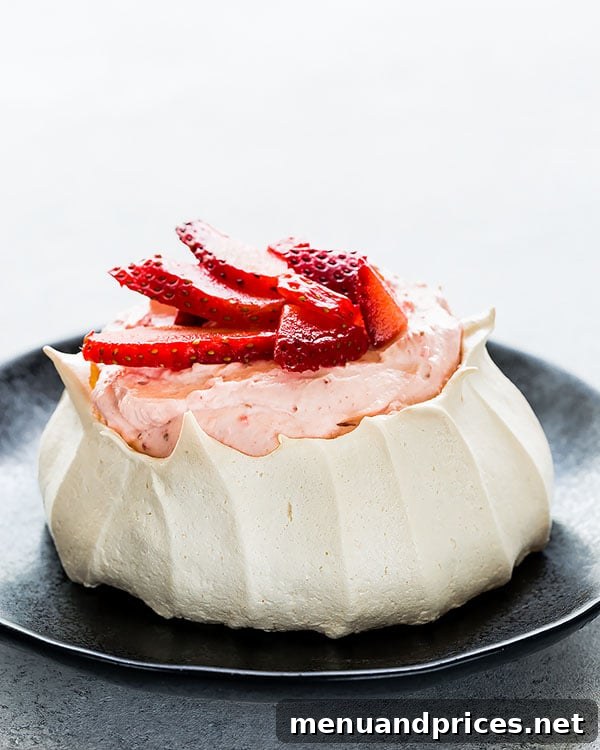 A single mini strawberry pavlova on a pristine white plate, garnished with freshly sliced strawberries and a dusting of powder.