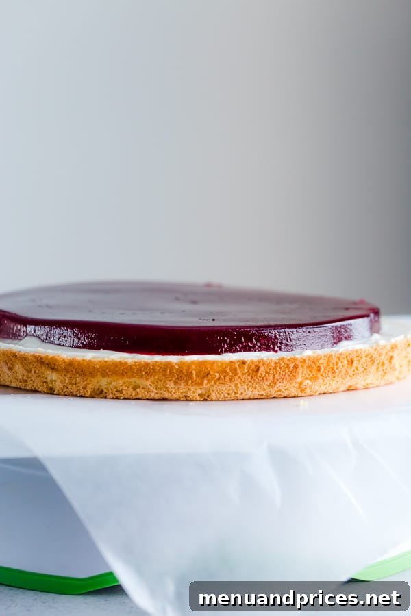 A vibrant raspberry jello layer placed between cake and frosting, ready for the next layer.