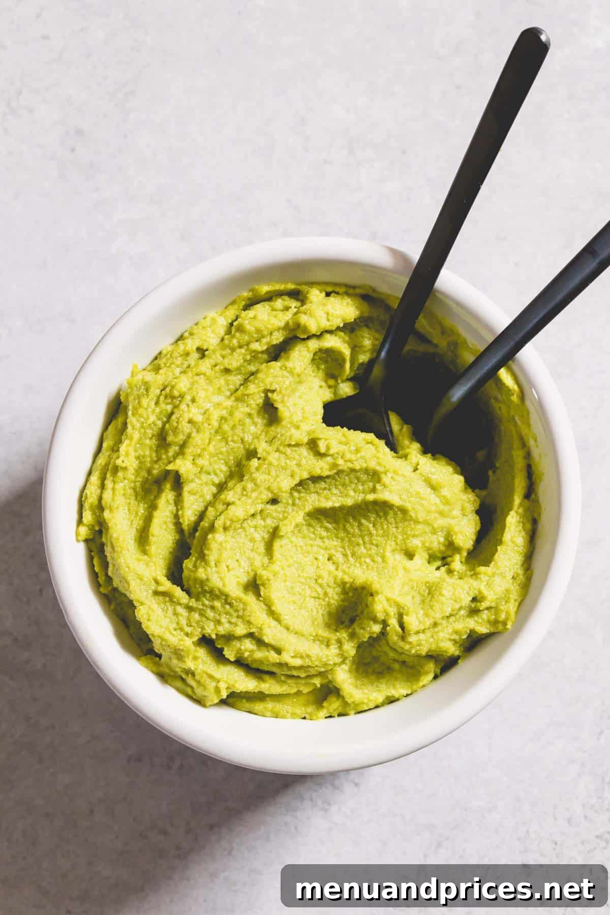 Easy Homemade Pistachio Paste Recipe 9 Smooth pistachio paste presented in a white bowl with two spoons, highlighting its inviting texture.