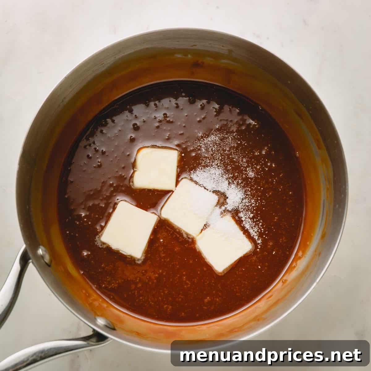 Mastering Dry Caramel Sauce 8 Four slices of room-temperature butter and a sprinkle of coarse sea salt being added to the cooled caramel sauce in the pot.