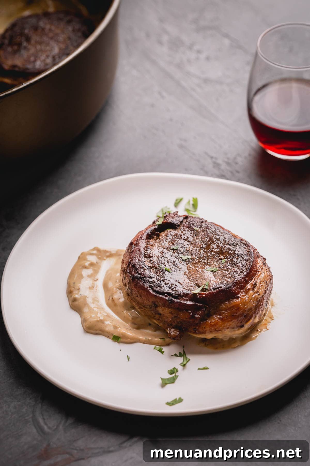 A whole bacon wrapped filet mignon steak with white sauce on a white plate.