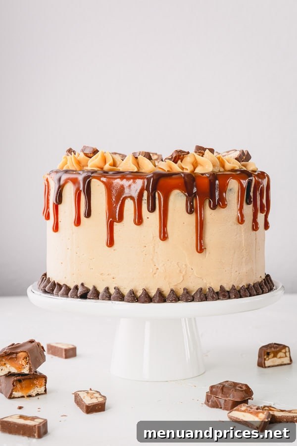 A whole Snickers cake decorated with caramel sauce, ganache and slices of snickers bar.