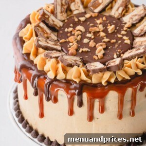 A whole Snickers cake decorated with caramel sauce, ganache and slices of snickers bar.