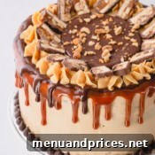 A whole Snickers cake decorated with caramel sauce, ganache and slices of snickers bar.